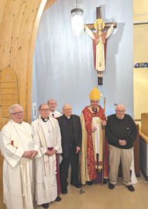 a group of clergy stand below a statue of Jesus on a wall in a church